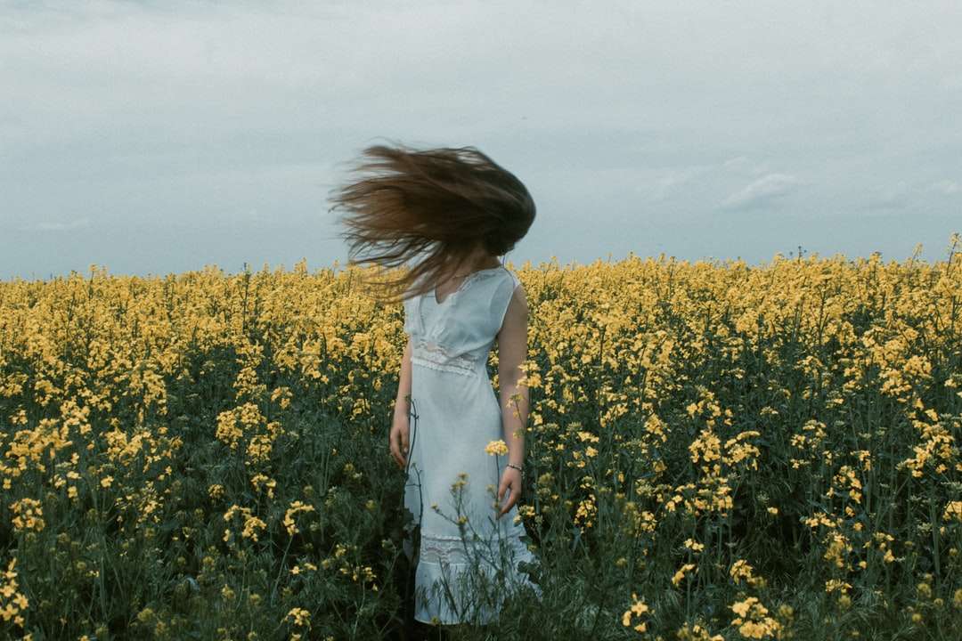 Mujer en vestido blanco de pie en campo de flores amarillo rompecabezas en línea