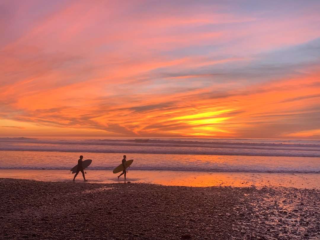 2 людини гуляють по пляжу під час заходу сонця онлайн пазл