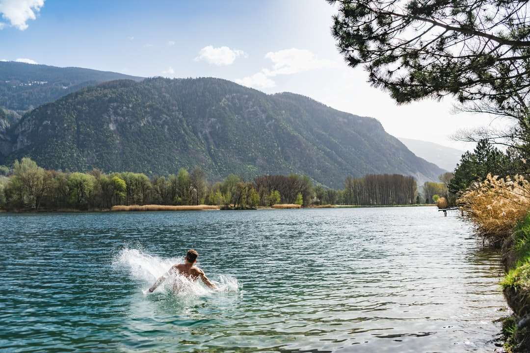Kvinna i vit klänning på vatten nära gröna träd och berg Pussel online