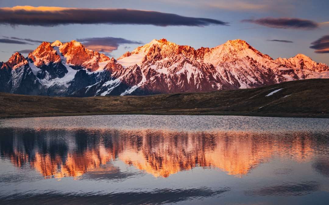 Mountain maro și alb lângă lac sub cer gri puzzle online