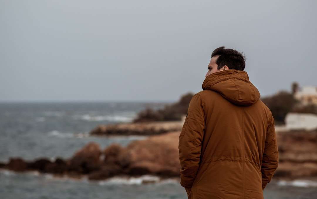 Uomo in felpa con cappuccio marrone in piedi vicino al corpo d'acqua puzzle online