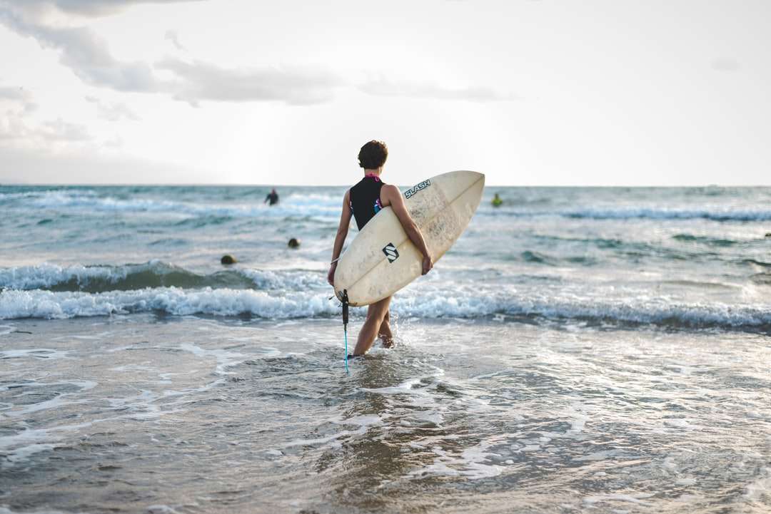 Man in zwarte wetsuit draagt ​​witte surfplank legpuzzel online