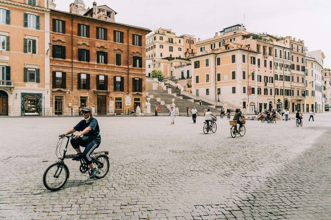 Oamenii de echitatie de bicicleta pe drumul in apropierea cladirii de beton maro puzzle online