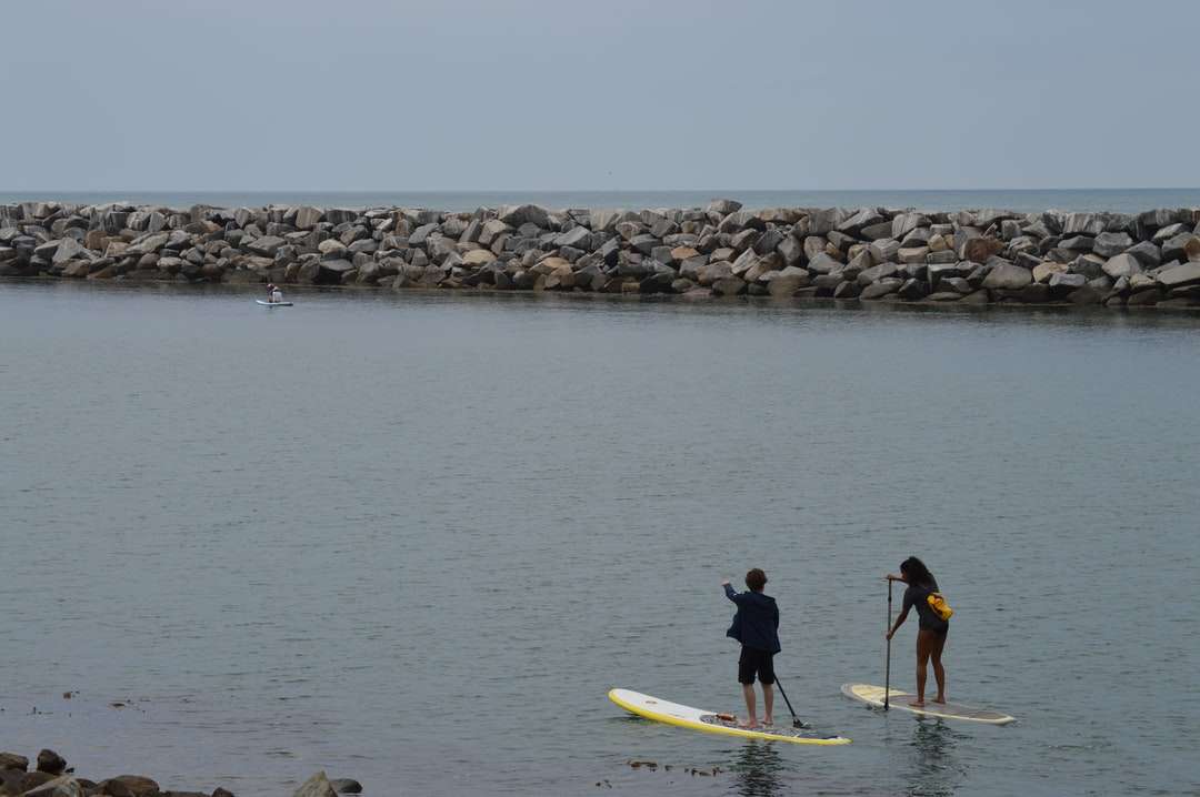мъж и жена в черен мокър костюм, каращи жълта дъска за сърф онлайн пъзел