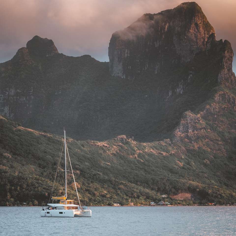 Barca albă pe corpul de apă lângă munte în timpul zilei puzzle online