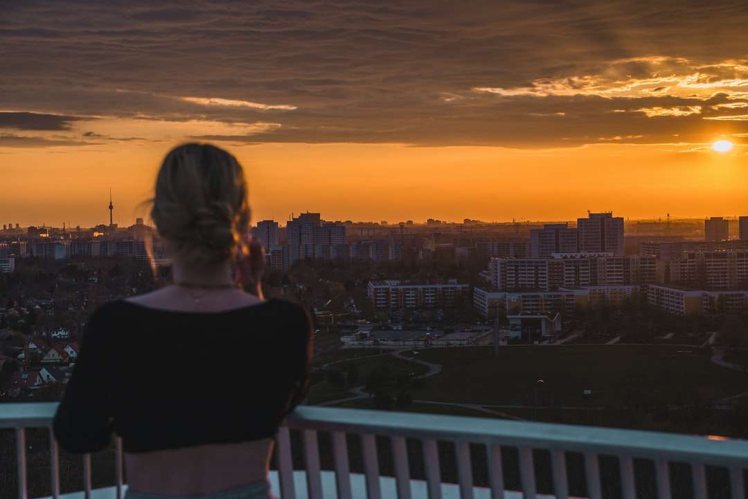 Kvinna i svart skjorta som står på balkongen under solnedgången pussel på nätet