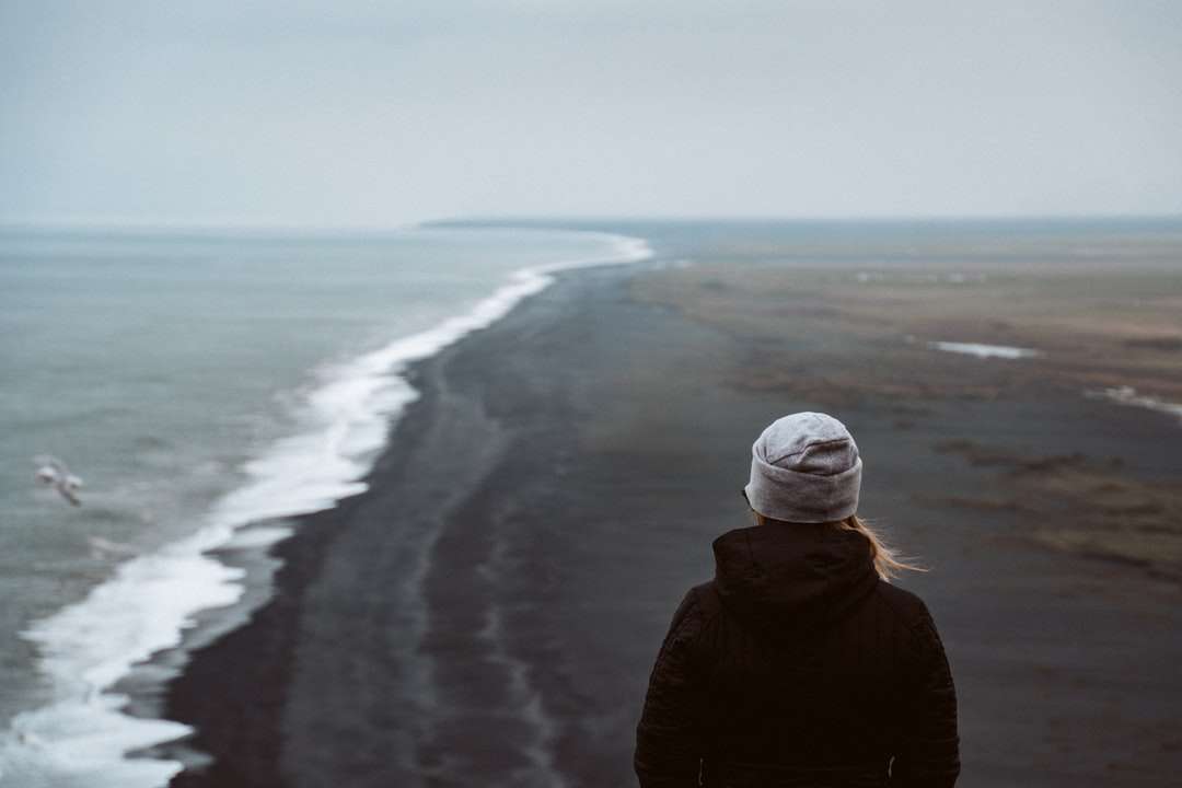 Osoba v černé bundě stojící na pobřeží během dne online puzzle