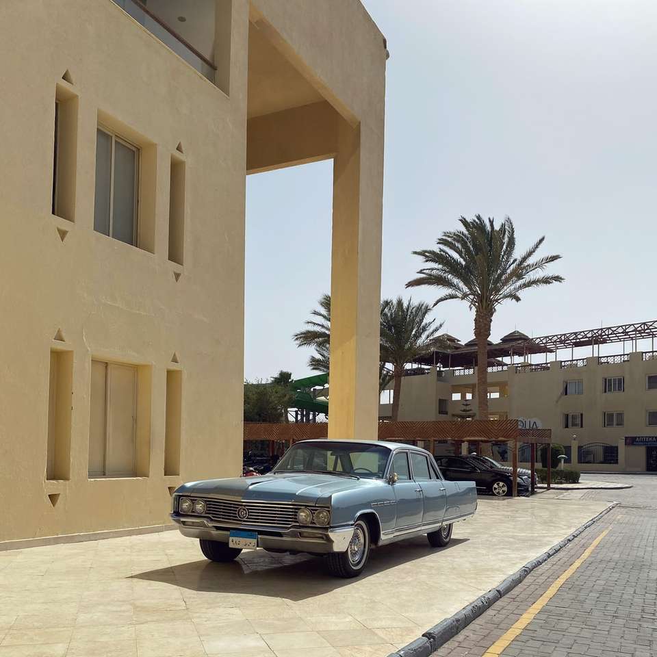 Black Sedan parcheggiato accanto all'edificio in cemento beige puzzle online