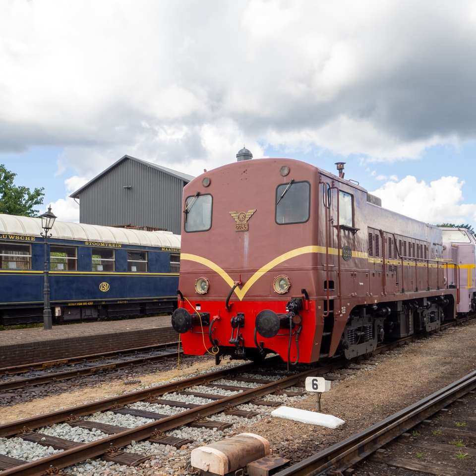 Blå och rött tåg på järnvägsspår under molnig himmel pussel på nätet