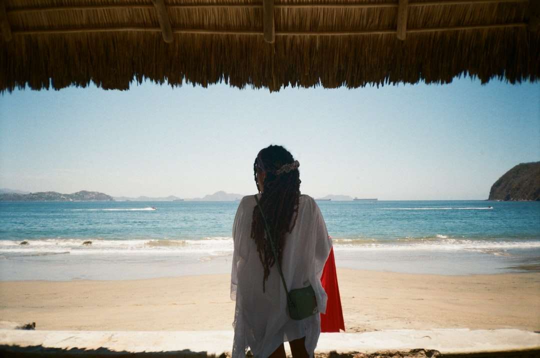 Hombre en chaqueta blanca y roja de pie en la playa durante el día rompecabezas en línea