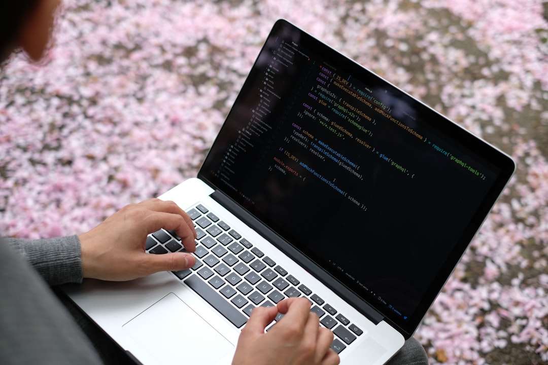 person som använder macbook pro på rosa och vit blommig textil pussel på nätet