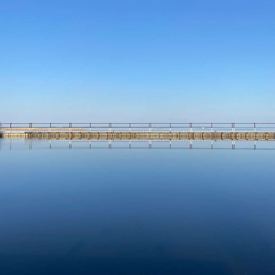 Weißes hölzernes Dock auf ruhigem Wasser unter blauem Himmel Puzzlespiel online
