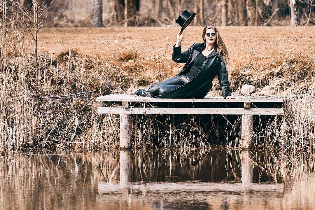 Kvinna i svart jacka sitter på vit träbänk Pussel online