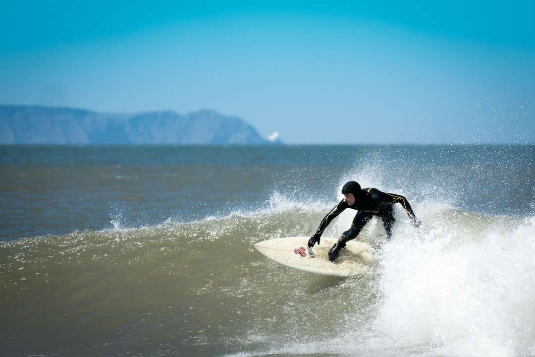 мъж в черен хидрокостюм, сърфиращ в морето през деня онлайн пъзел