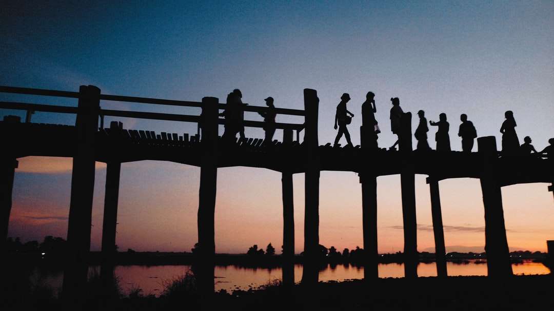 Silueta de personas de pie en el muelle de madera durante la puesta del sol rompecabezas en línea