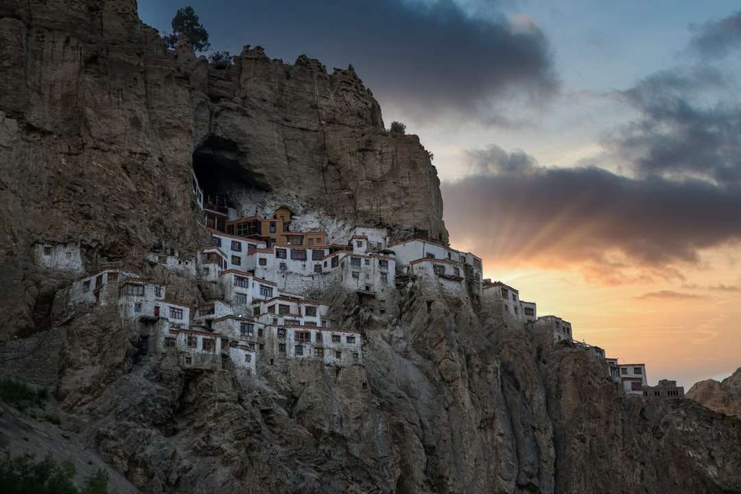 Edifício de concreto branco na montanha rochosa sob o céu nebuloso puzzle online