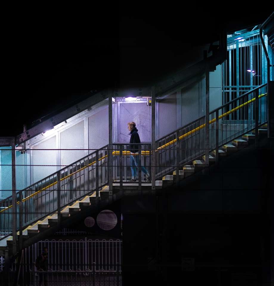Човек в черно яке стои на черен метален мост онлайн пъзел