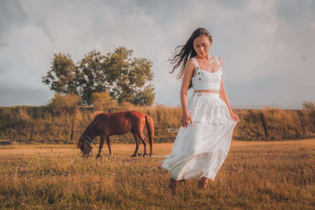 Kvinna i vit klänning som står bredvid brun häst Pussel online