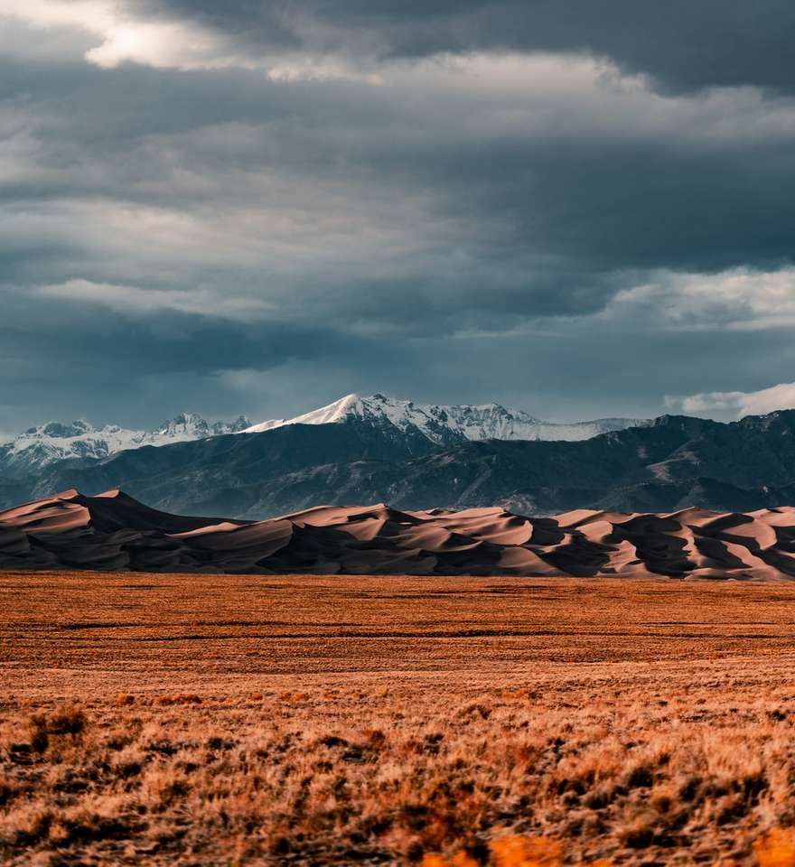 brown field near snow covered mountains under cloudy sky online puzzle