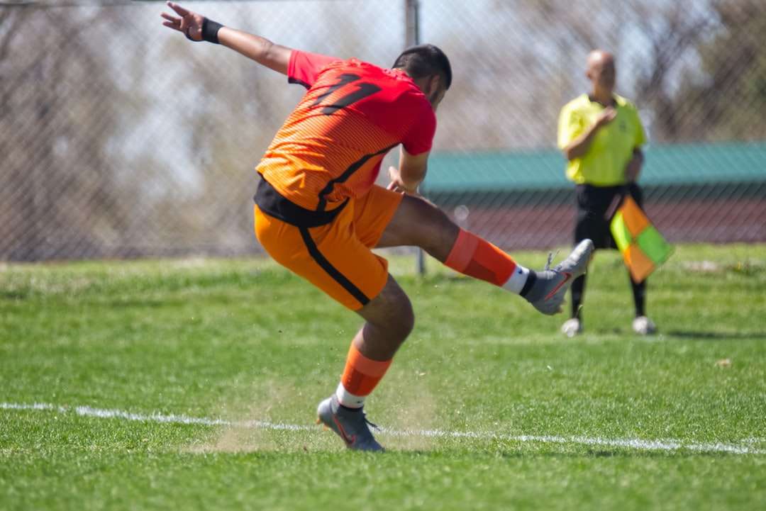 Hombre en camisa de jersey naranja pateando el balón de fútbol rompecabezas en línea