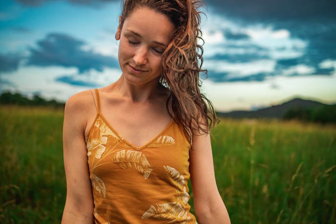 Mujer en camiseta amarilla de tanque de pie en campo de hierba verde rompecabezas en línea
