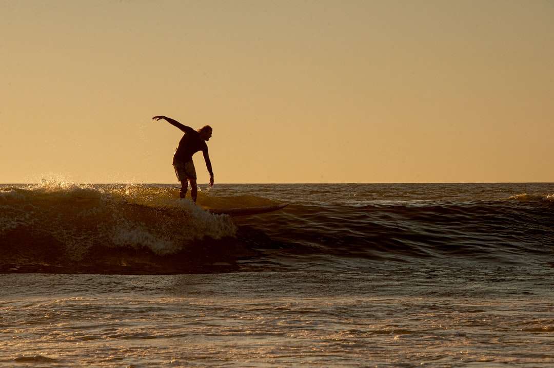 Hombre en pantalones cortos negros surf en el mar durante el día rompecabezas en línea