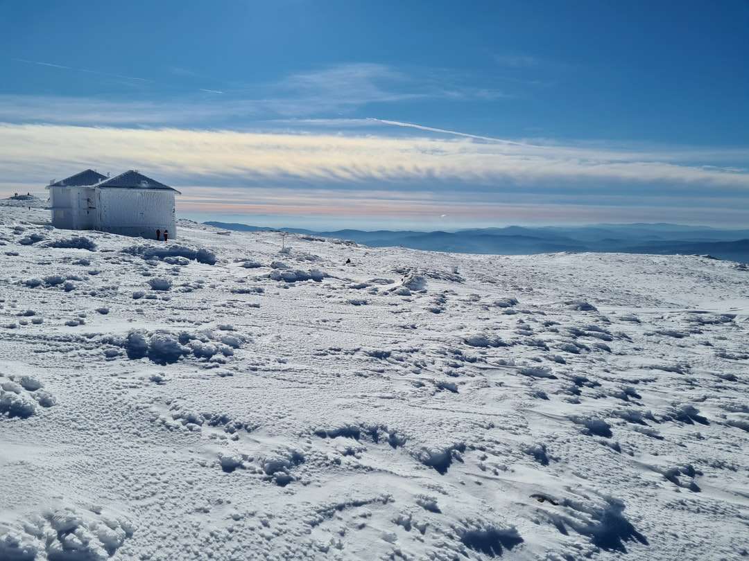 青空の下で雪に覆われた地面に白と灰色の家 オンラインパズル