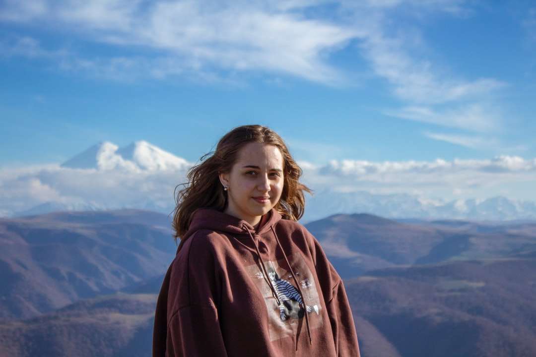 Γυναίκα σε κόκκινο hoodie στέκεται στην κορυφή του βουνού online παζλ