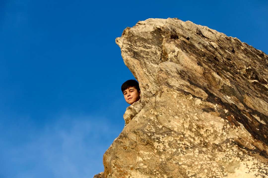 Kvinna i brun jacka som står på bergformation pussel på nätet