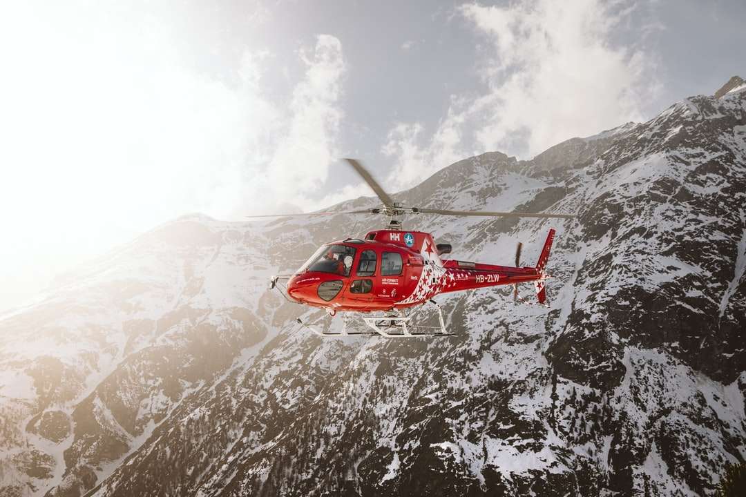 Червен и бял хеликоптер, плаващ над покритата сняг планина онлайн пъзел