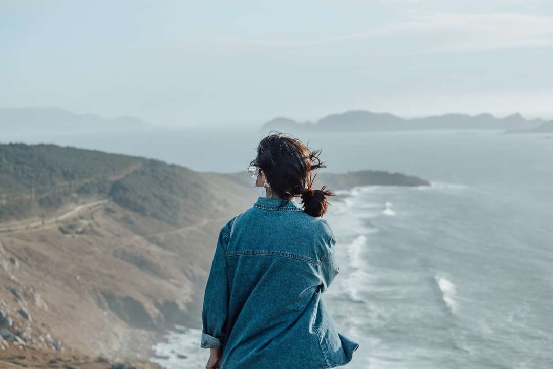 femme en veste en jean bleu debout sur la falaise pendant la journée puzzle en ligne