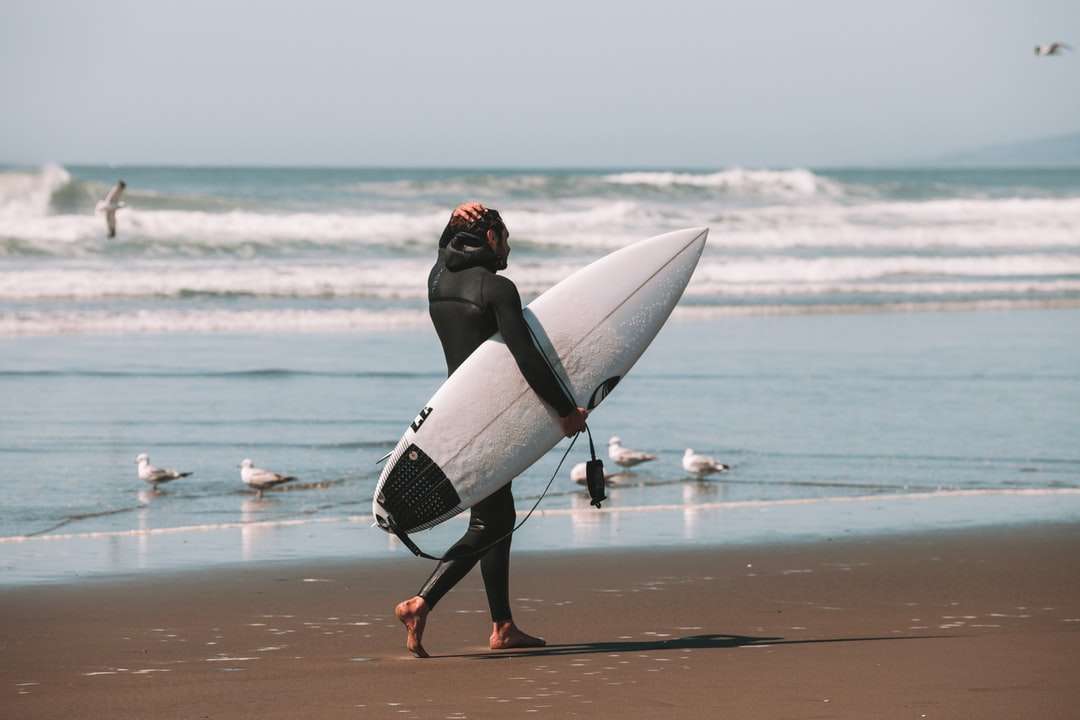 Frau im schwarzen Neoprenanzug, der weiße Surfbrett hält Online-Puzzle