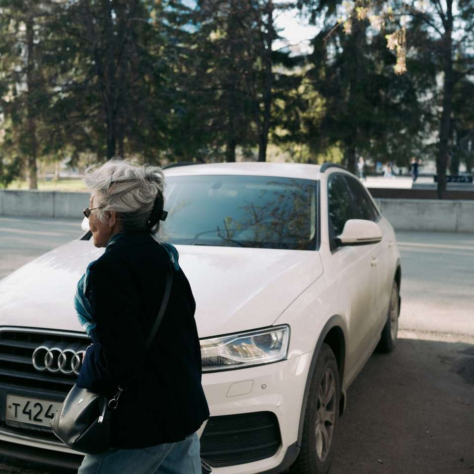 Mujer en chaqueta negra de pie junto al coche Audi blanco rompecabezas en línea