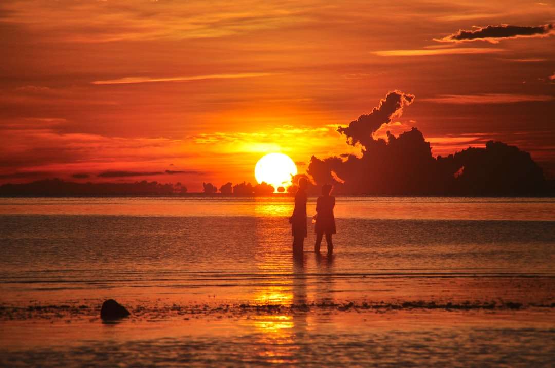 Silueta de 2 personas de pie en la playa durante la puesta del sol. rompecabezas en línea