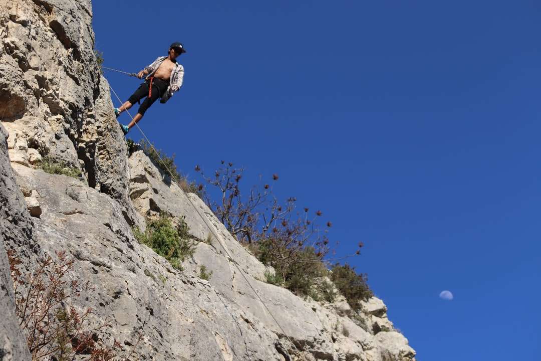 Man i blå jacka klättring på stenigt berg under dagtid Pussel online