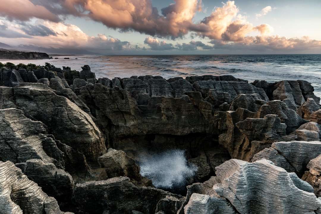 Montanha rochosa marrom perto de ondas do mar durante o dia quebra-cabeças online