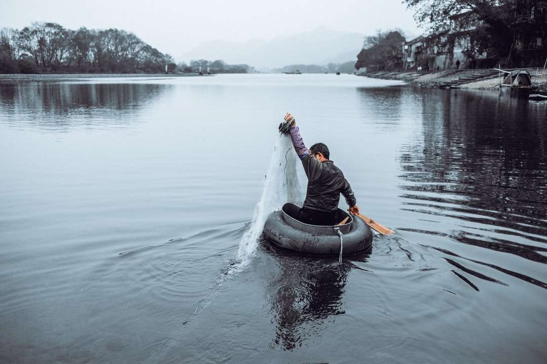 Hombre en chaqueta negra montando en kayak blanco en cuerpo de agua rompecabezas en línea
