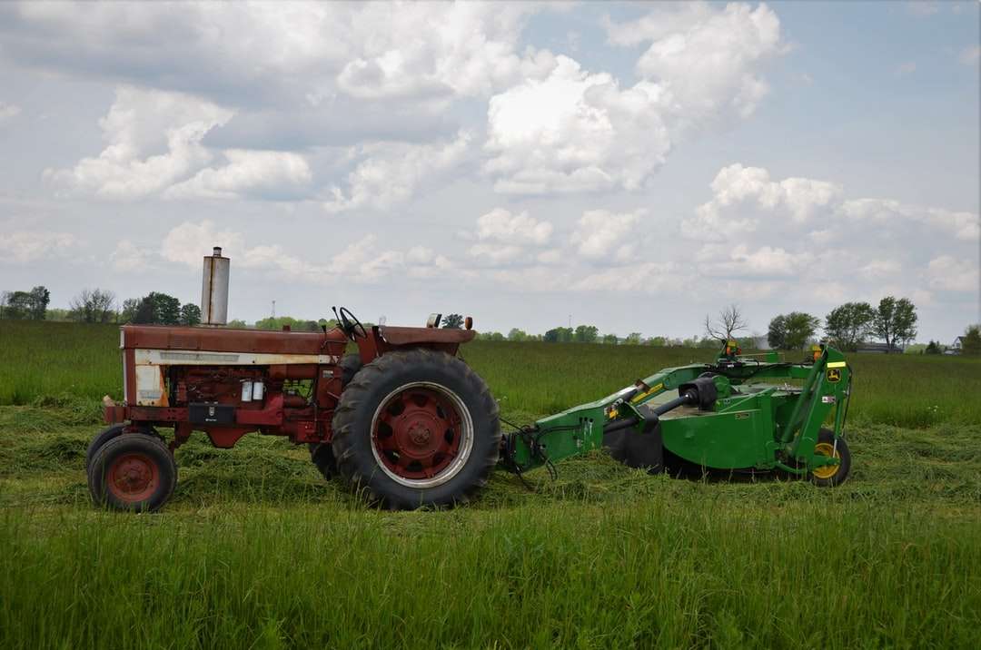 Rode tractor op groen grasveld onder witte wolken legpuzzel online
