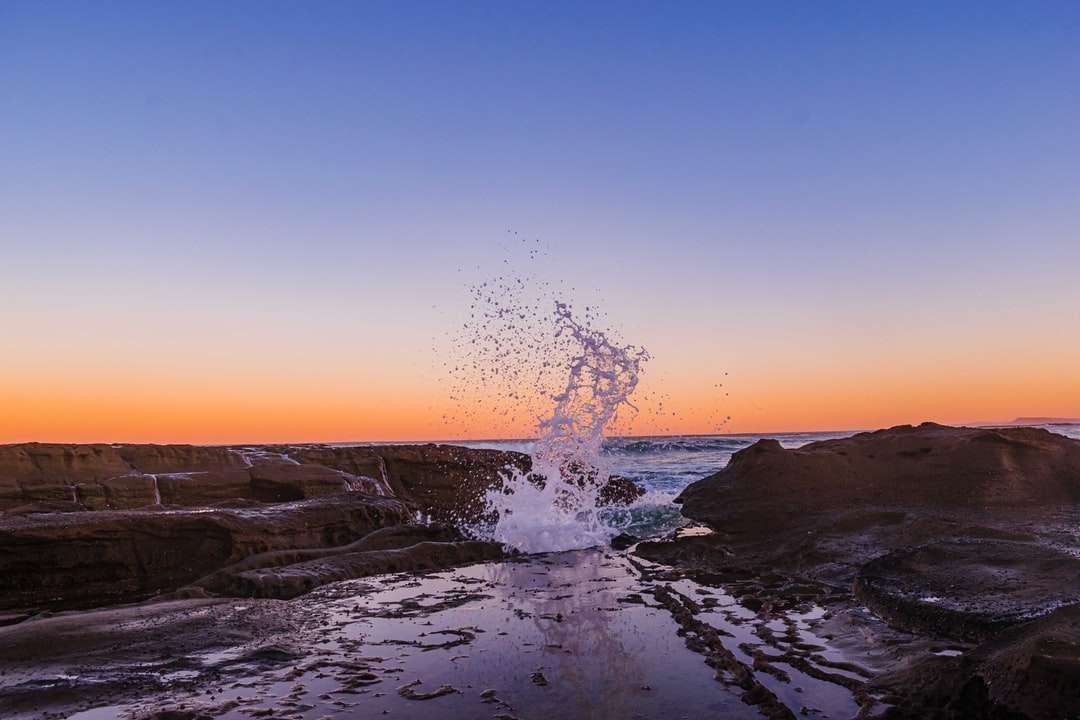 Vattenstänk på stenig strand under solnedgången pussel på nätet