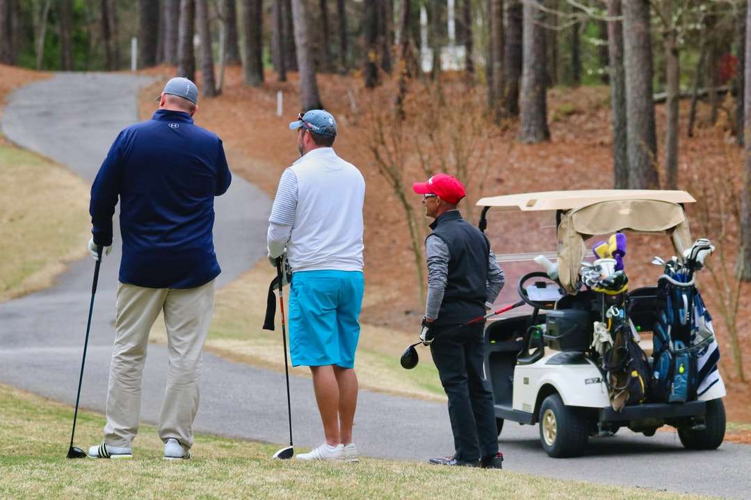 Трое мужчин в белой форме едут на тележке для гольфа в дневное время. онлайн-пазл