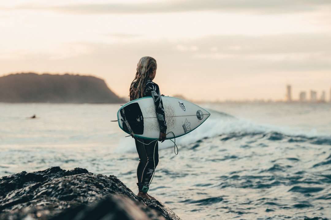 kvinna i svart våtdräkt bär vit surfbräda pussel på nätet