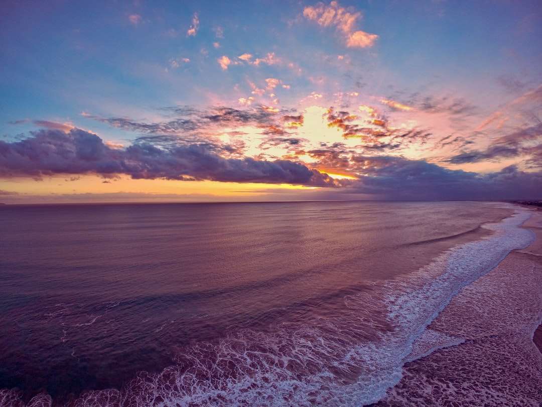 havsvågor kraschar på stranden under solnedgången Pussel online