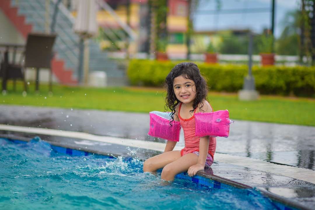 Chica en camisa rosa sentado en piscina azul rompecabezas en línea