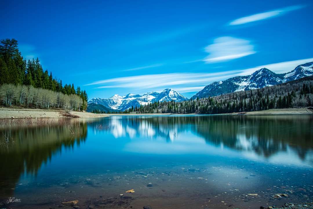 Lago rodeado por árvores verdes e montanhas sob o céu azul puzzle online