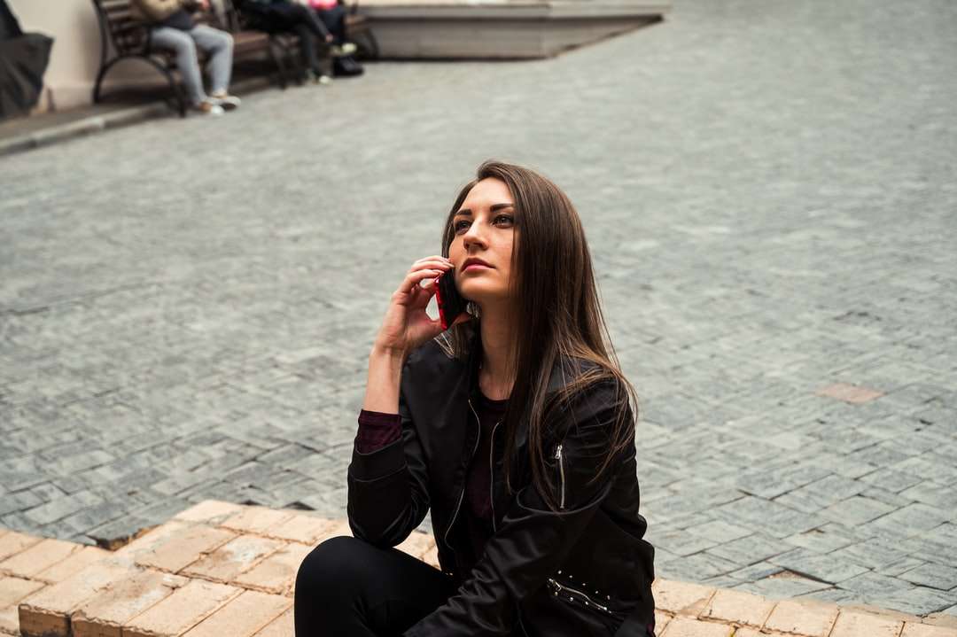 Mulher no casaco de couro preto sentado no chão de tijolo marrom quebra-cabeças online
