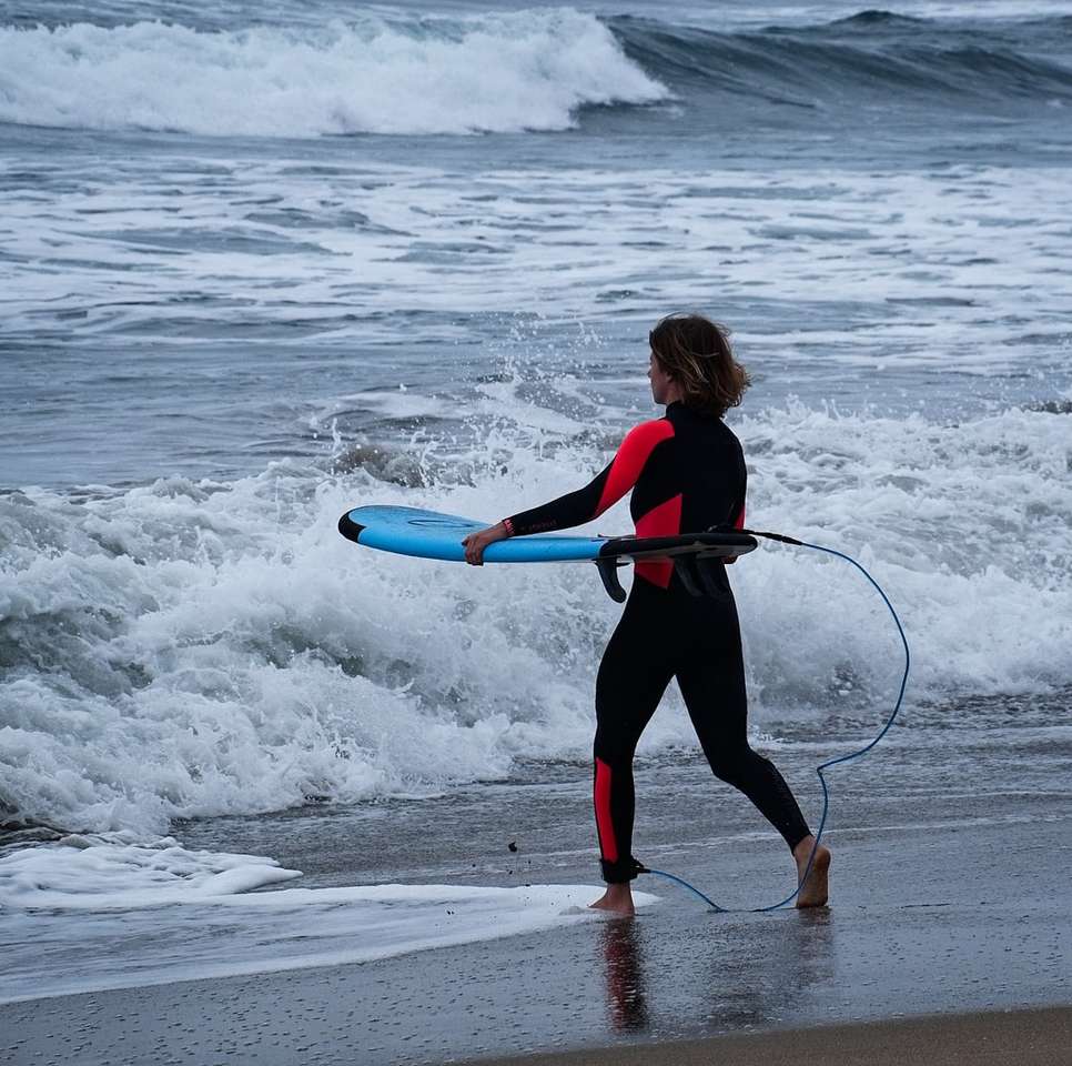 жінка в чорно-червоній куртці тримає синю дошку для серфінгу пазл онлайн