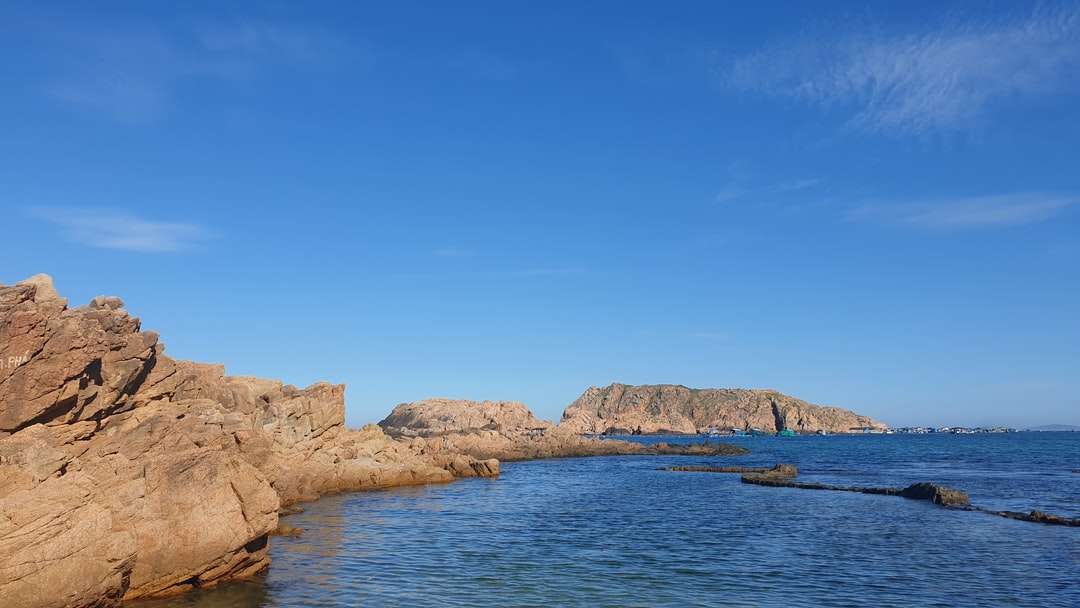 Hnědá skalní formace vedle modré moře pod modrou oblohou online puzzle