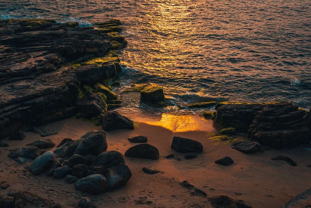 Rocas marrones en la orilla del mar durante la puesta del sol rompecabezas en línea