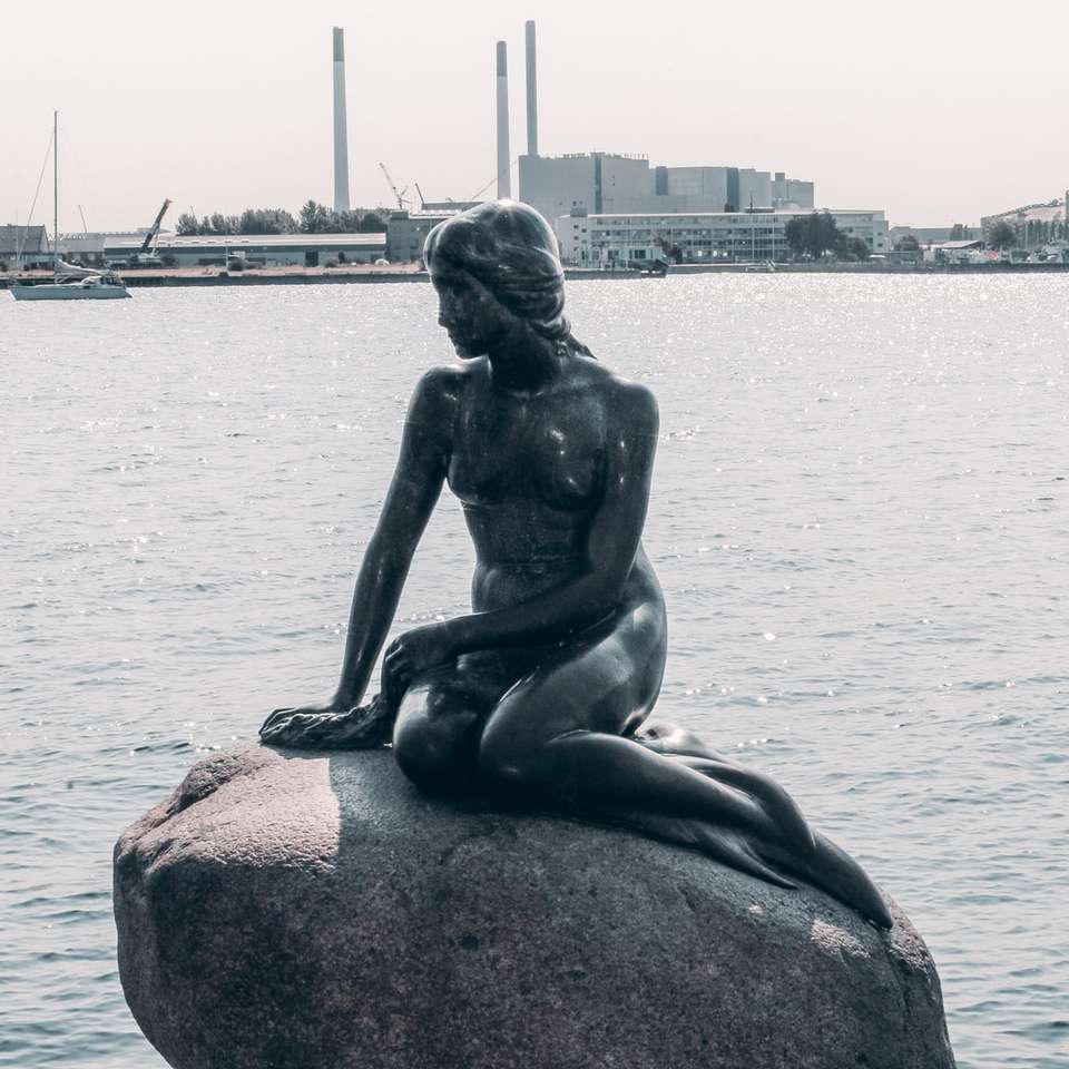 Statue der Frau, die auf Felsen nahe Körper des Wassers sitzt Online-Puzzle