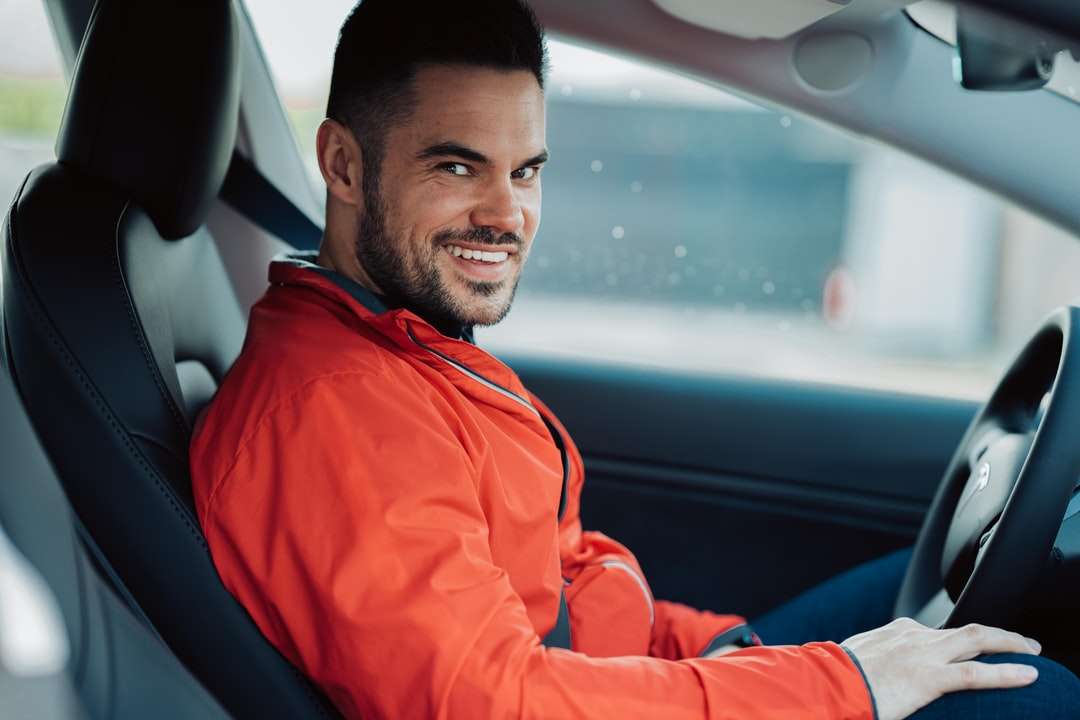 Mann in orangefarbener Jacke sitzt auf Autositz Puzzlespiel online